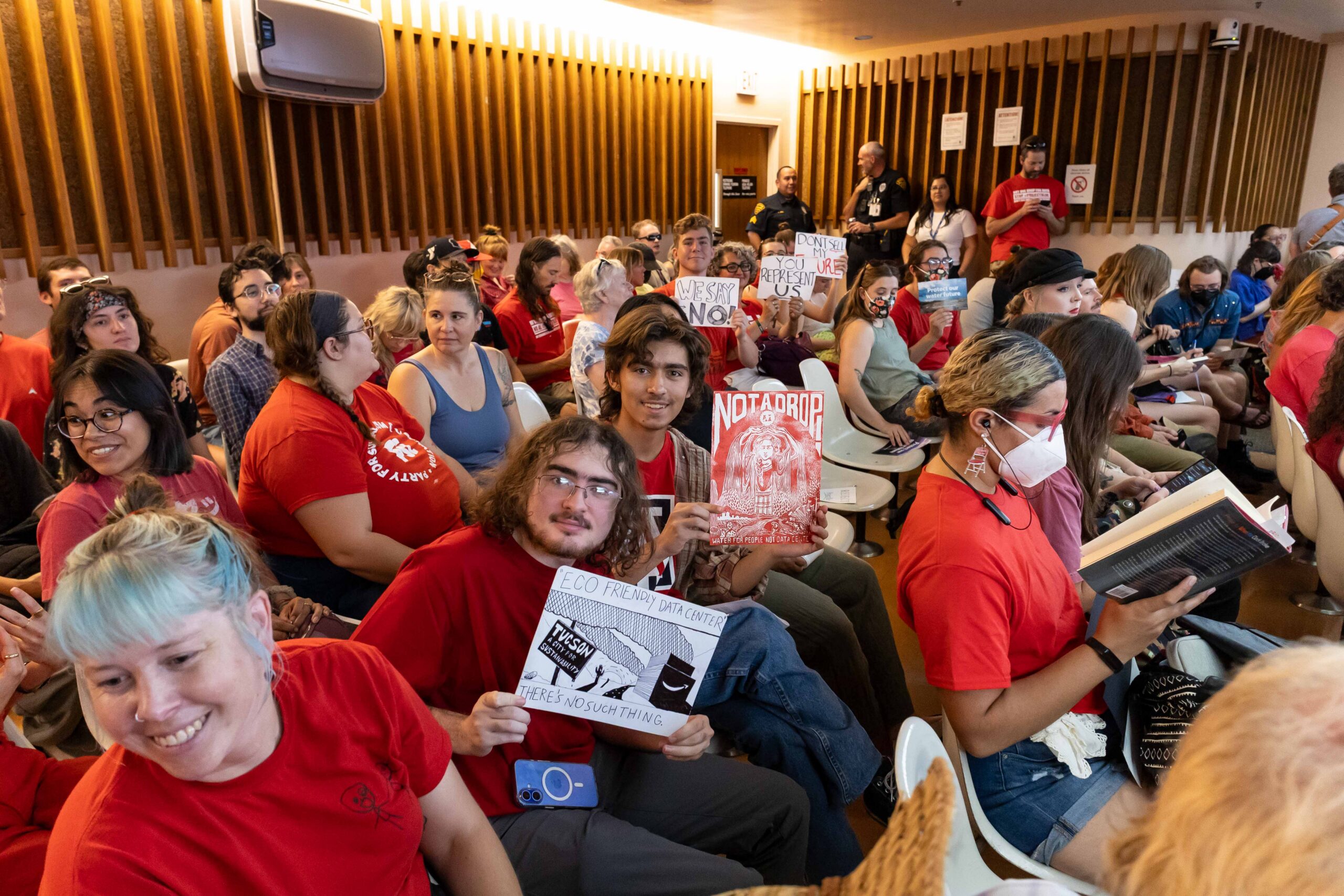 A group of people in red hold signs while sitting in a committee meeting
